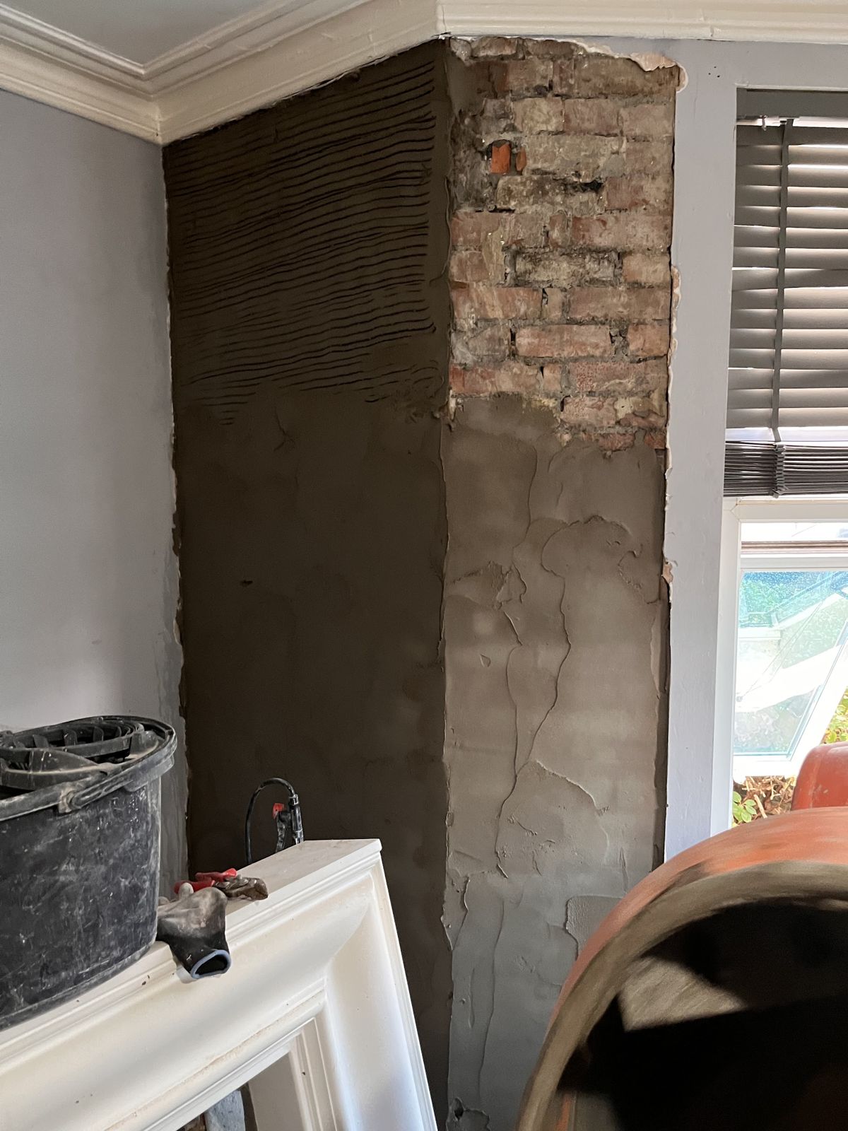 A chimney breast mid-job with fresh scratch-coat render beside bare brick