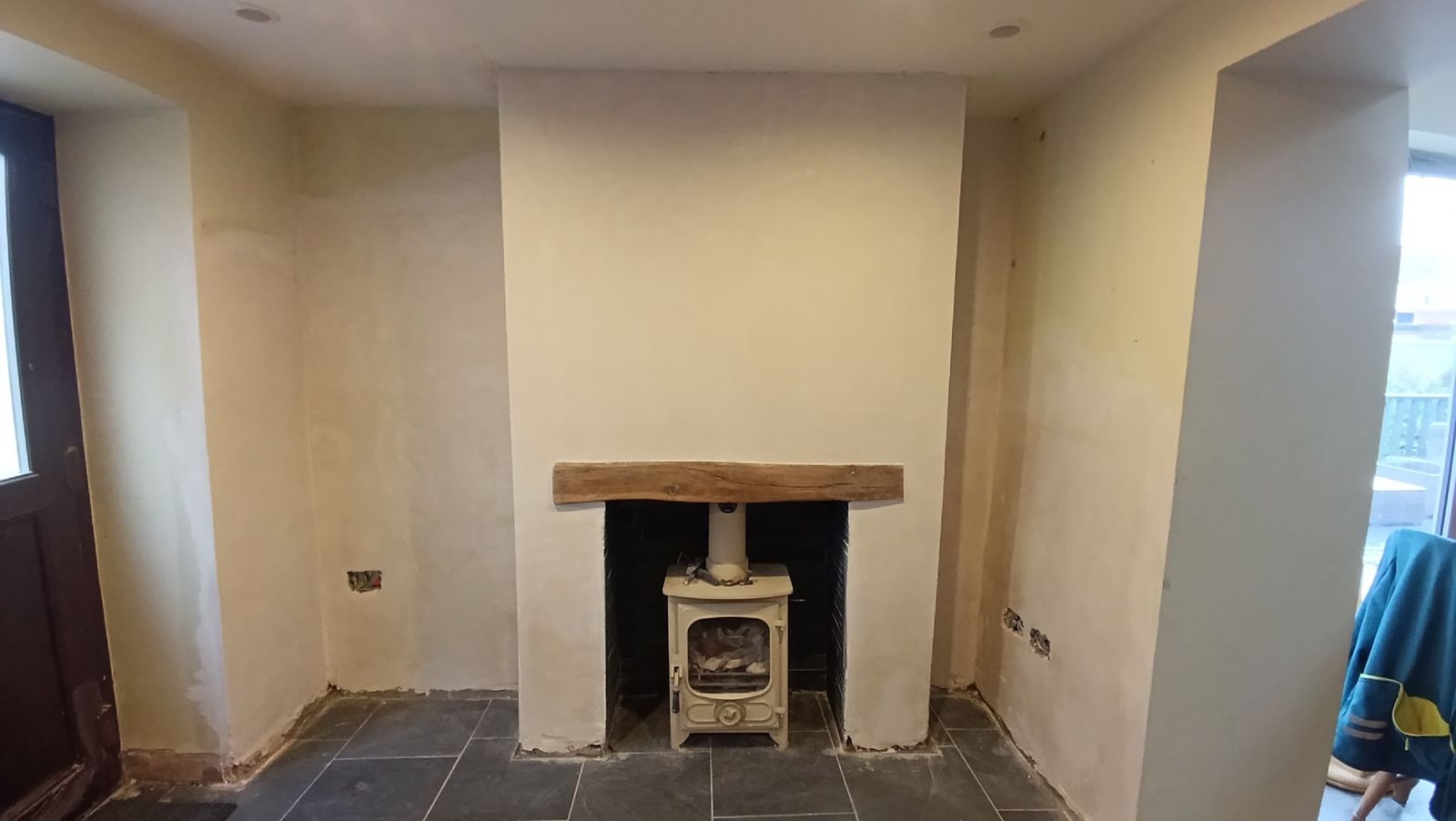 A finished room with freshly plastered walls, chimney breast and alcoves, an oak beam and a cream log burner