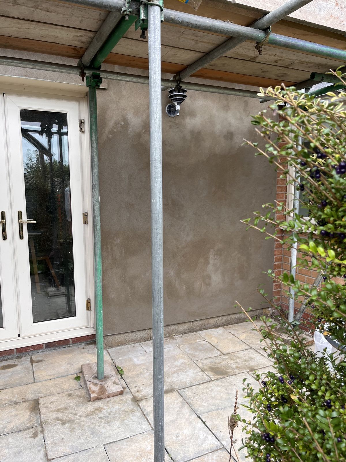 A freshly rendered exterior wall under scaffolding beside French doors