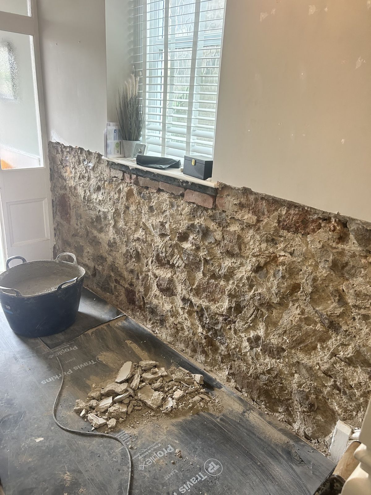 An old stone wall exposed below a window after the plaster has been hacked off