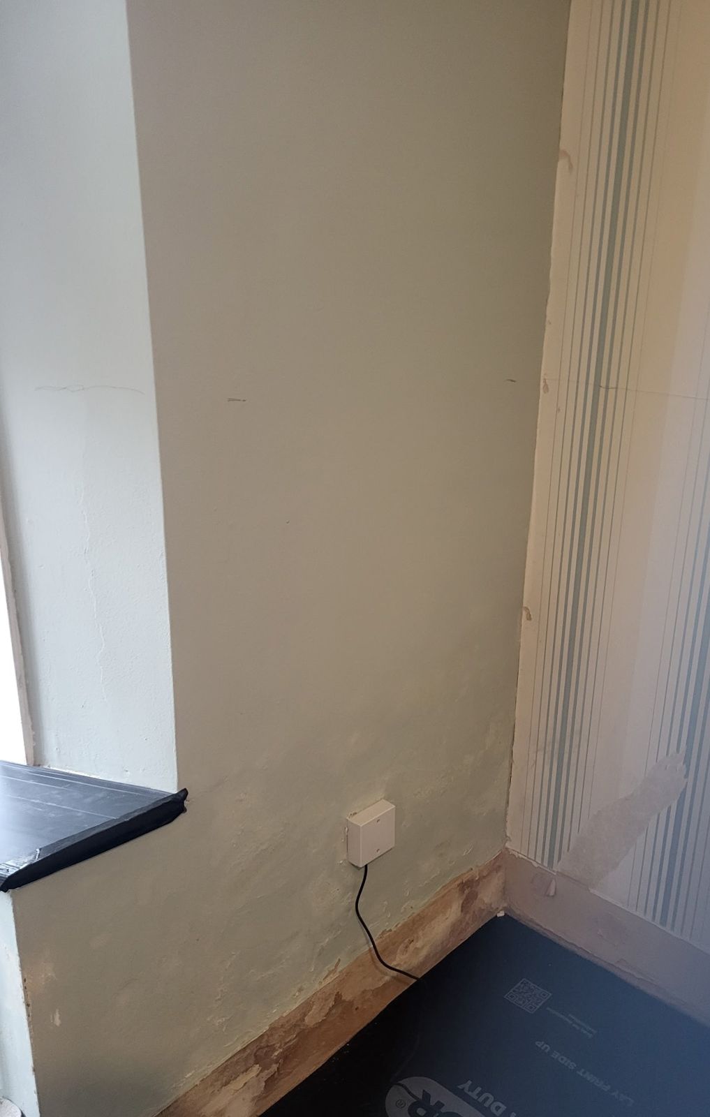 A damp-damaged corner of a room with perished skirting and blown paint