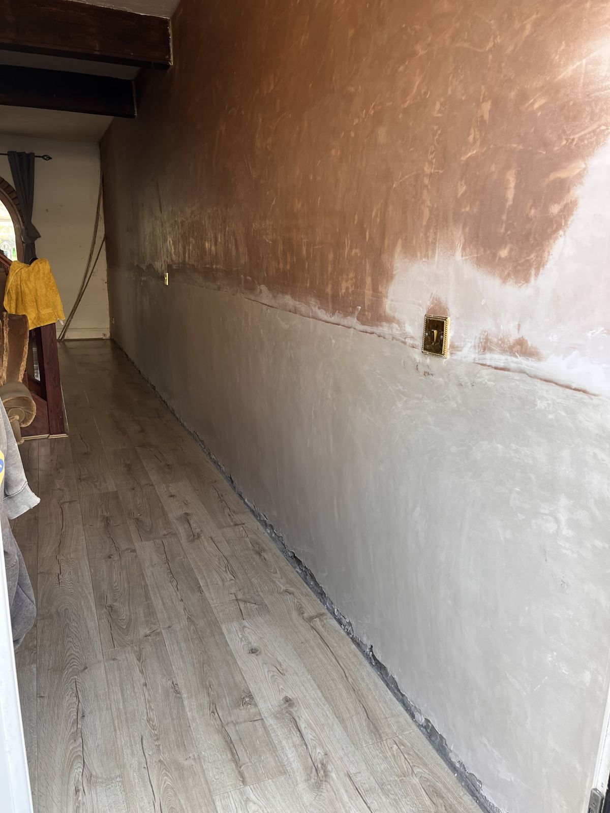 A long hallway wall freshly re-plastered, with new plaster on the lower section meeting a skimmed upper section