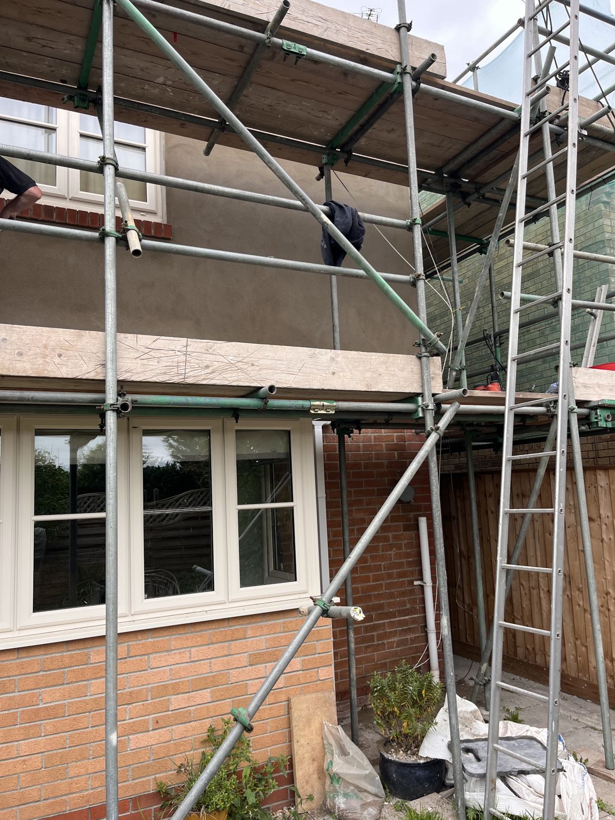 The back of a house under scaffolding with its first-floor wall freshly rendered