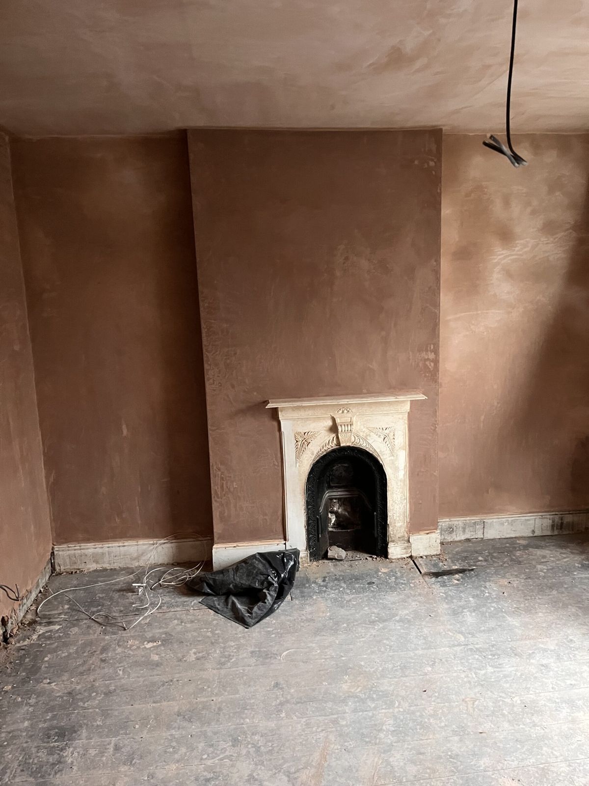 A room freshly plastered from floor to ceiling around a Victorian cast-iron fireplace