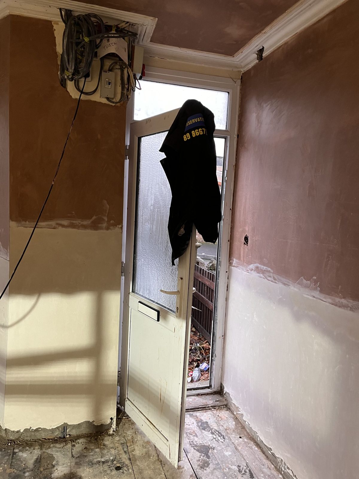 A hallway mid-job with new plaster to dado height and a black S&C Preservations work jacket hanging on the door